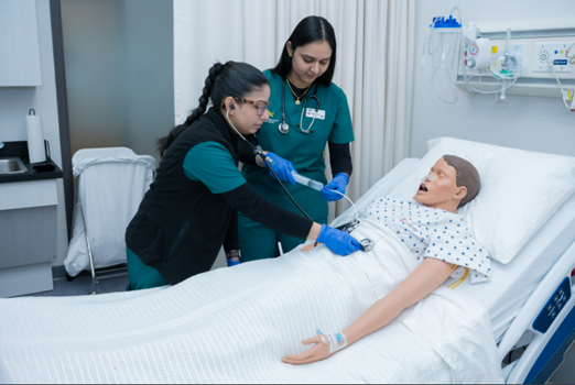 Two student nurses in simulation lab, attending to patient. 