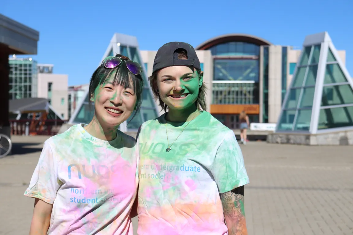 Two students in white shirts, covered in colour cornstarch, smiling sunning day