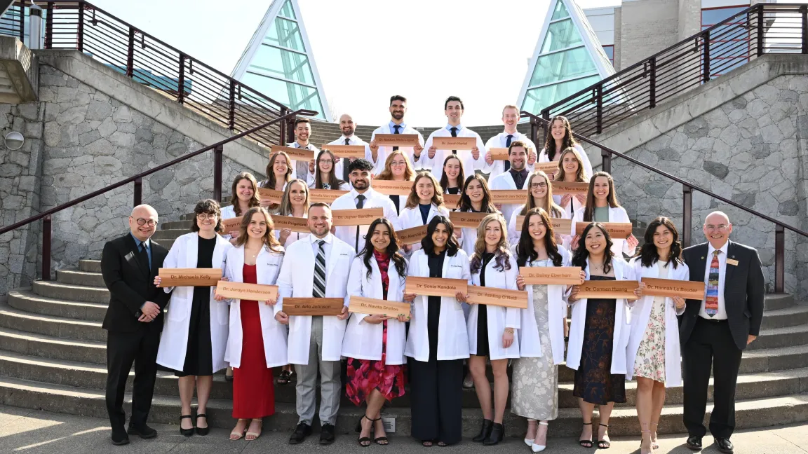 28 NMP graduates stand together on UNBC's Agora steps holding their cedar shingles.
