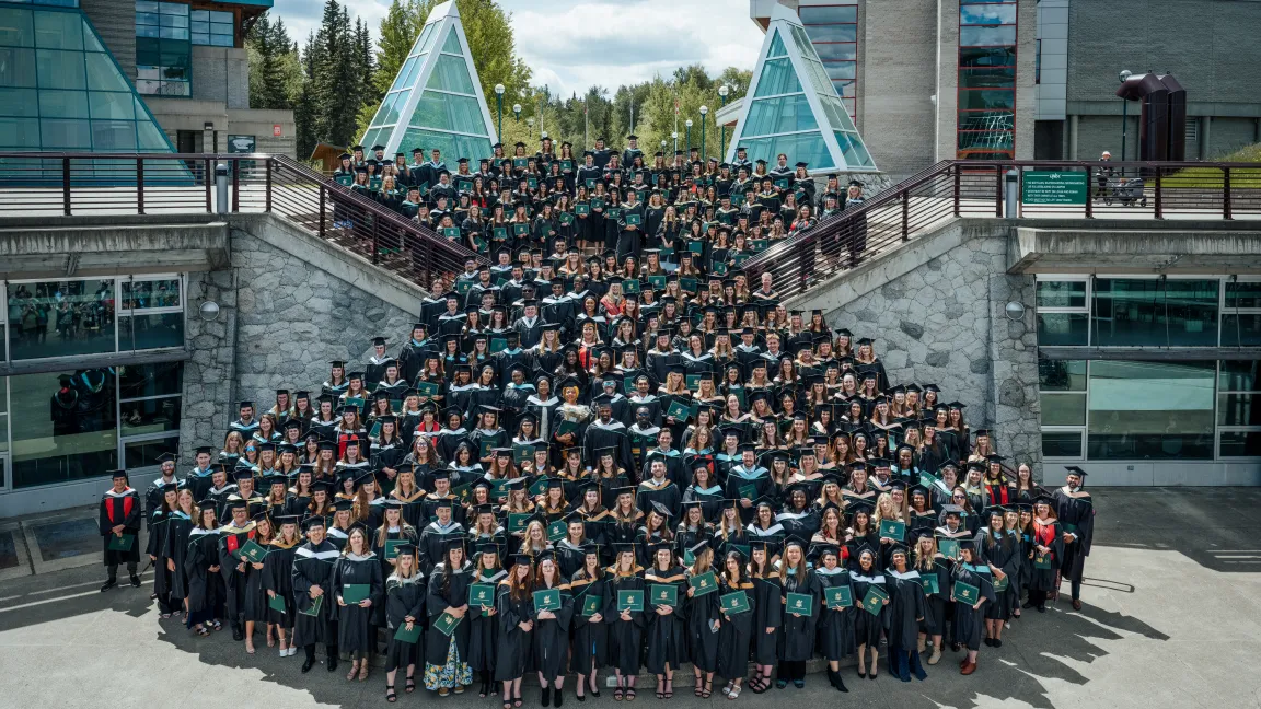Large group of graduates gathered for class photo outside in UNBC's Agora Courtyard.