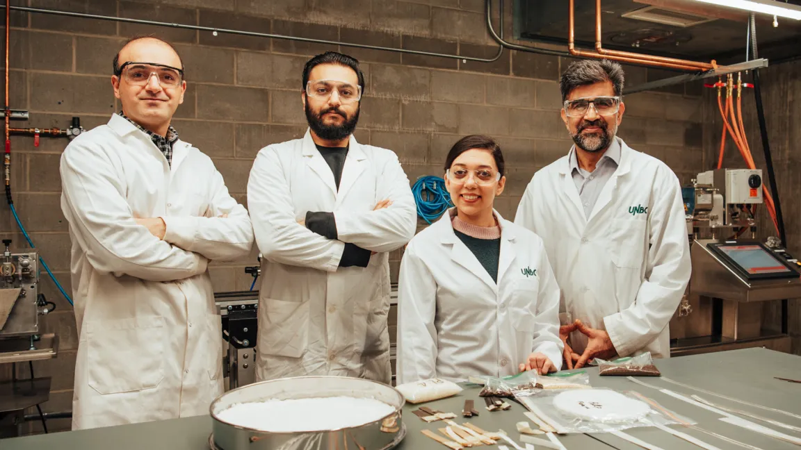 Four researchers in white lab coats standing behind a table displaying items in a laboratory