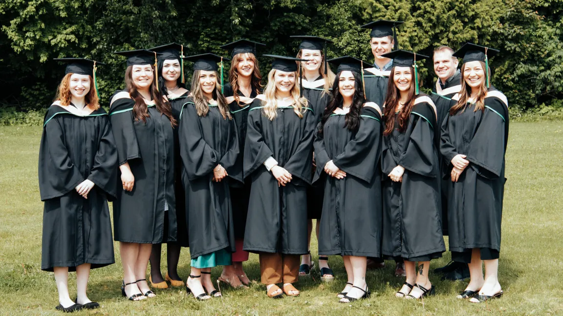 Large group of graduate students wearing black academic robes and mortarboards stands outdoors.