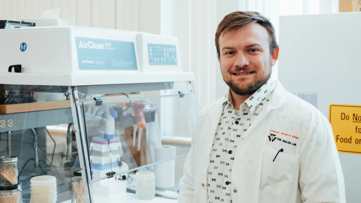 Dr. Jacob Walsh standing in his laboratory at UNBC, wearing a lab coat beside a biosafety workstation.
