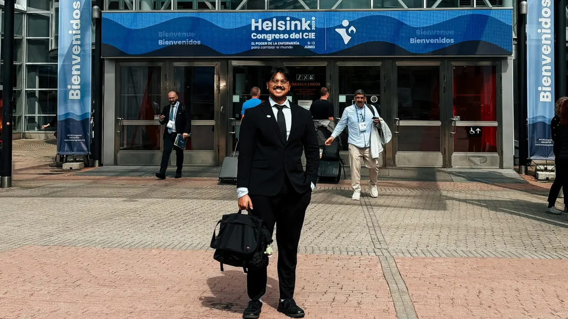 A person in a suit and tie holding a bag in front of a sign that says Helsinki