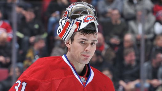 Person with a goalie mask perched on his head looks towards the camera. Person is wearing a red jersey with white and blue trim and the number 31 visible on the left side of the photo. Goalie mask is white with red and blue logo on it, chrome face shield and displays the number 31 in the centre.