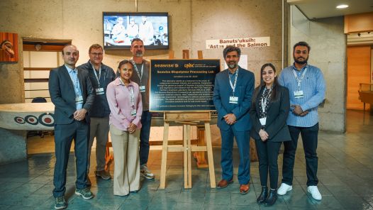 Group of seven people gather around an easel holding a plaque in UNBC's Robert Frederick Art Gallery.