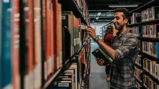 Two students looking at books on bookshelves in library
