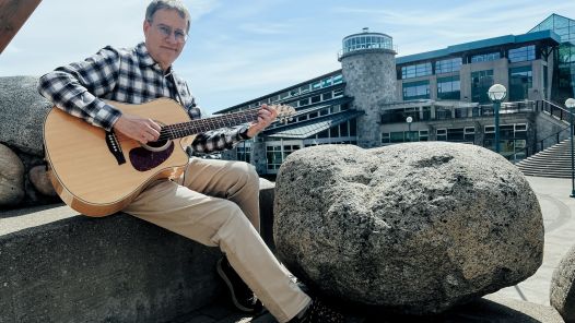 Dr. Kevin Hutchings with a guitar outside at UNBC's Prince George campus. 