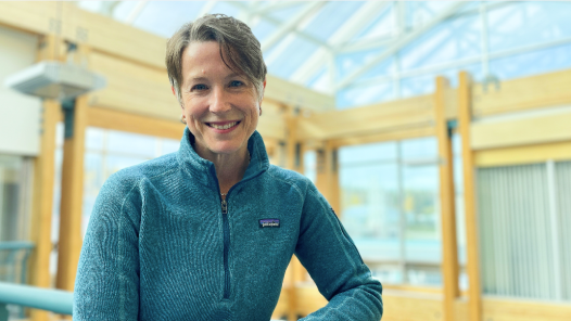 Women in long sleeve shirt stands in front of wood and glass background