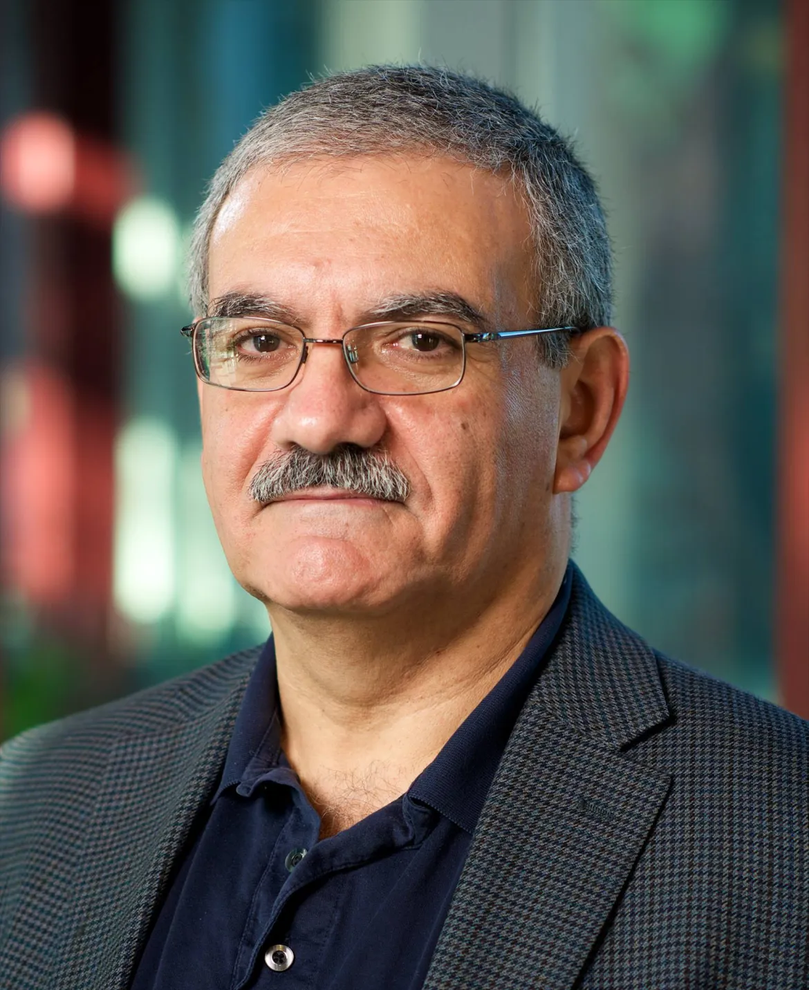 Dr. Elie Korkmaz, wearing a dark blazer and glasses, poses indoors against a softly blurred background.