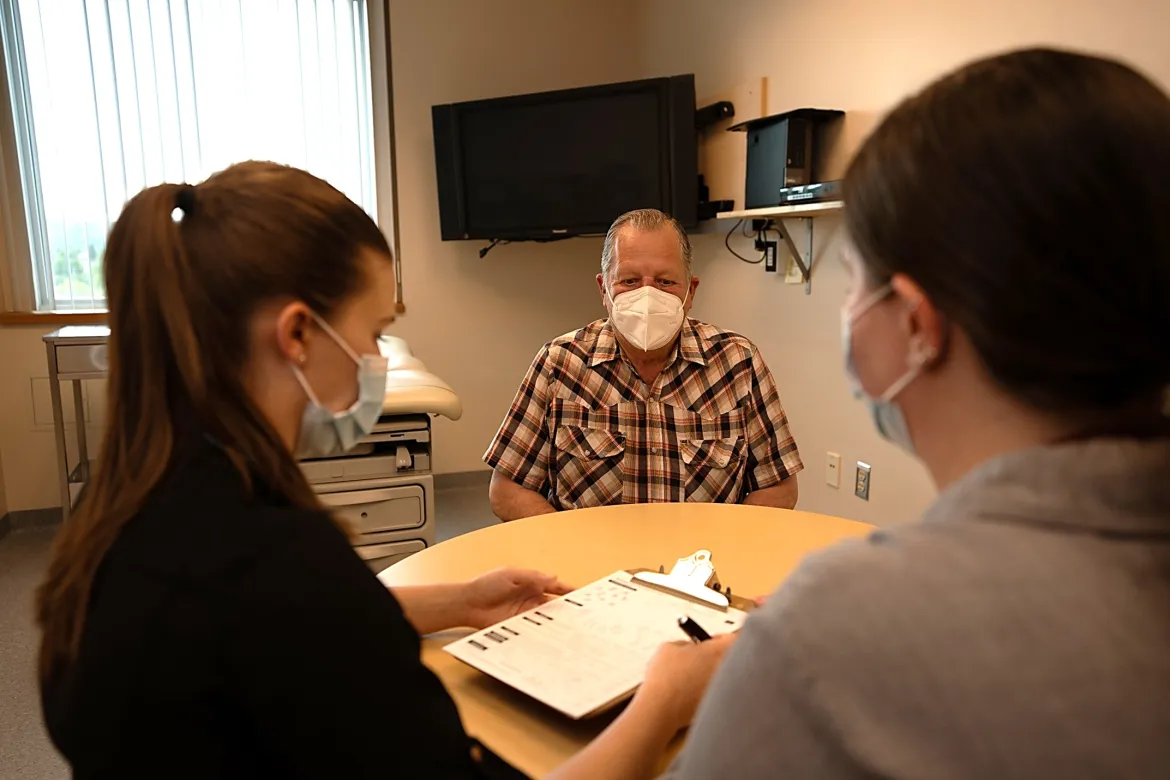 Two medical students and a First Patient Program volunteer sit together at a table, as one students reviews a questionnaire.