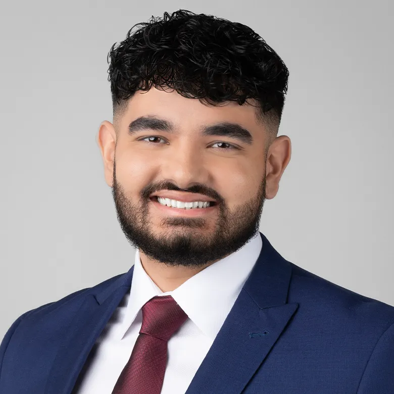 Jujhar Sandhu headshot, dressed in a navy suit with white shirt and burgundy tie