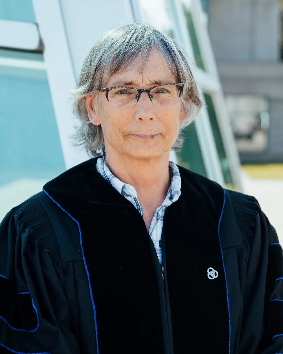 Dr. Kathy Lewis stands in academic regalia outside a UNBC building during the Professor Emeritus recognition event.