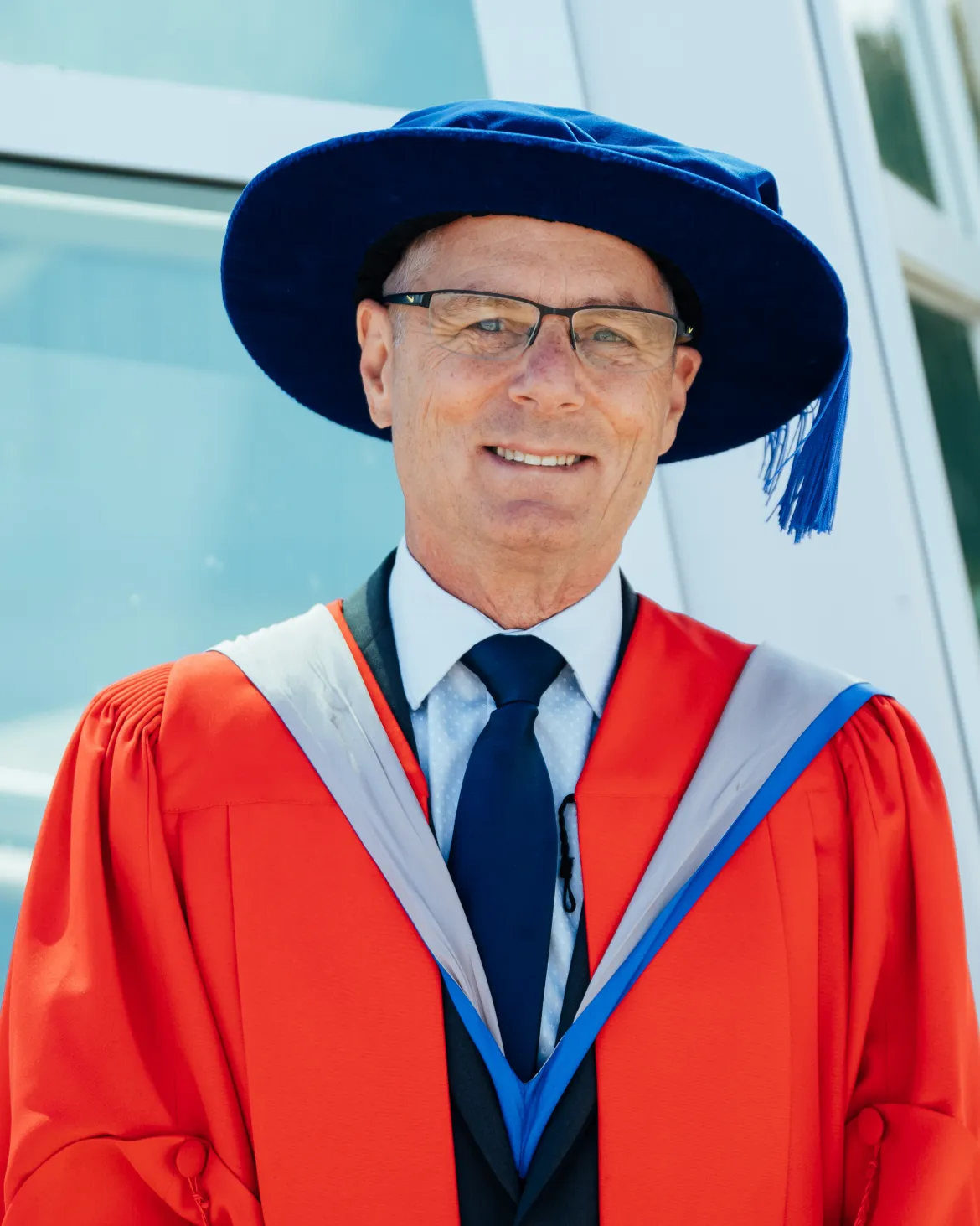 Dr. Kerry Reimer stands in academic regalia and ceremonial hat outside a UNBC building during the Professor Emeritus recognition event.