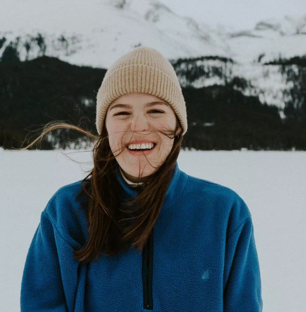 NMP Class of 2024 graduate Dr. Nora Morrison wears a toque and hoodie, and stands outdoors on snow with mountains in the background.