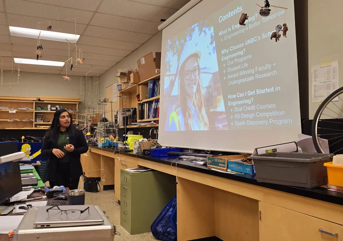 An Engineering professor stands by a projector screen in a high school classroom.