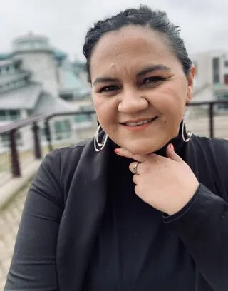 Photo of Penína Harding smiling, wearing a black top and beaded hoop earrings.