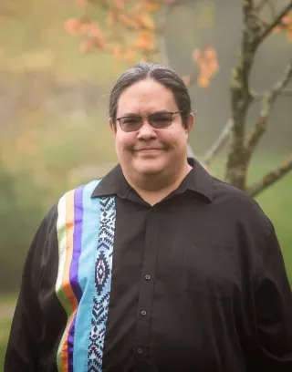Photo of Dr. Daniel Sims wearing a black button-down shirt with colorful vertical ribbons.