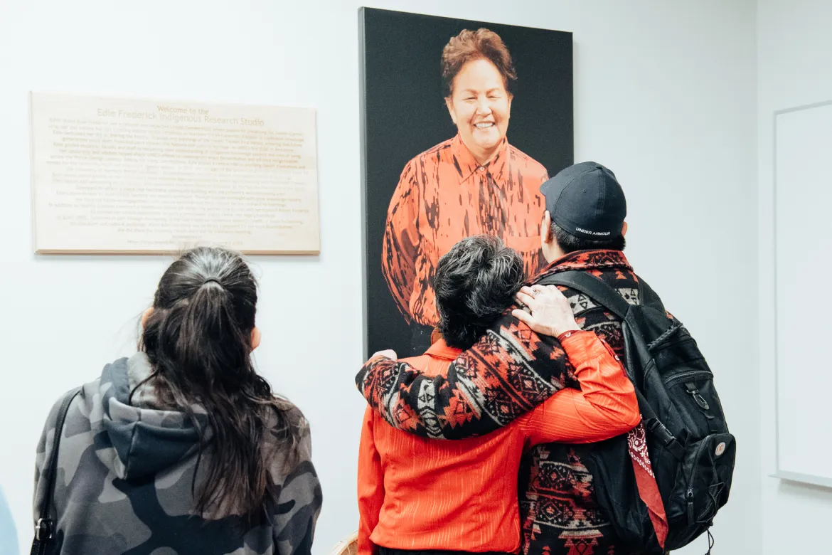 Three people look at a photo of the late Edie Frederick on the wall. 