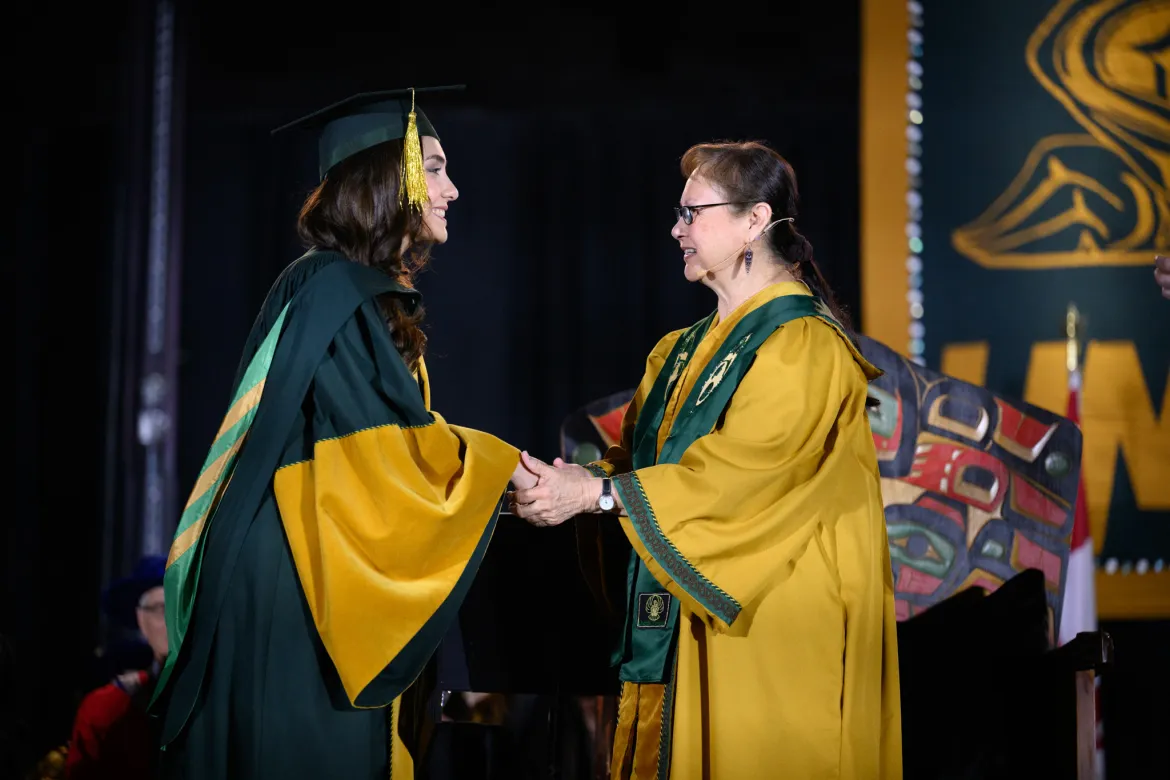 Two people in academic regalia shake hands at Convocation