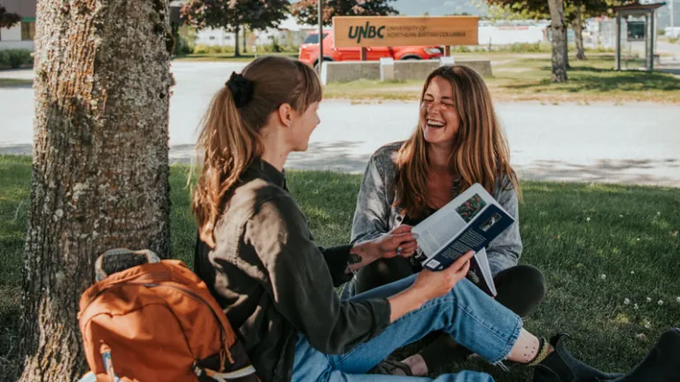 Two UNBC students sitting under a tree on campus