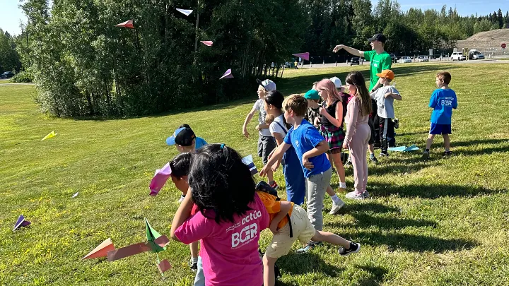 Group of kids and a camp leader throwing paper planes